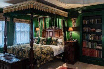 Photo of a hotel room at The Rookery in London featuring a luxurious four-poster bed, antique hardwood furniture, and dark green walls.
