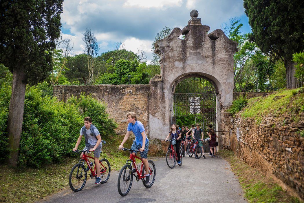 Young people on bicycles near a stone gate of the Calixtus Catacombs